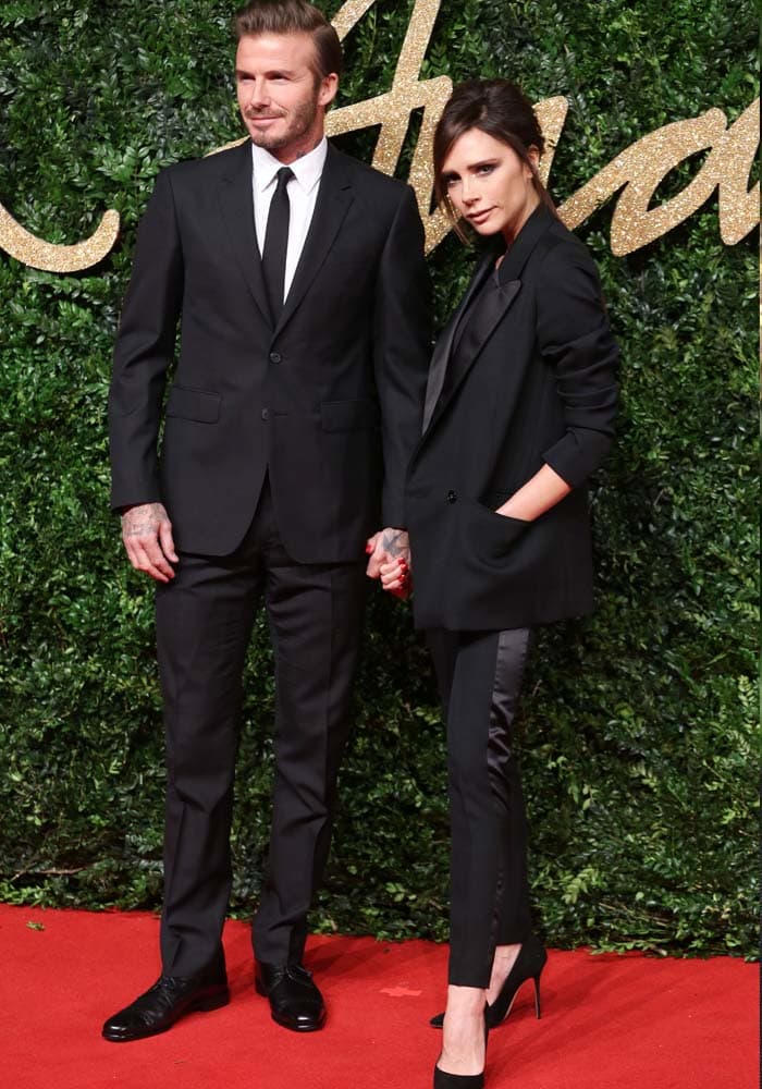 David Beckham and Victoria Beckham pose in matching tailored suits on the red carpet of the British Fashion Awards