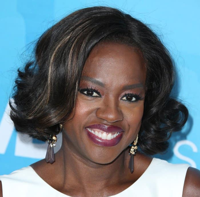 Viola Davis radiates elegance with her soft curls, deep berry lipstick, and glamorous eye makeup, perfectly complemented by statement earrings