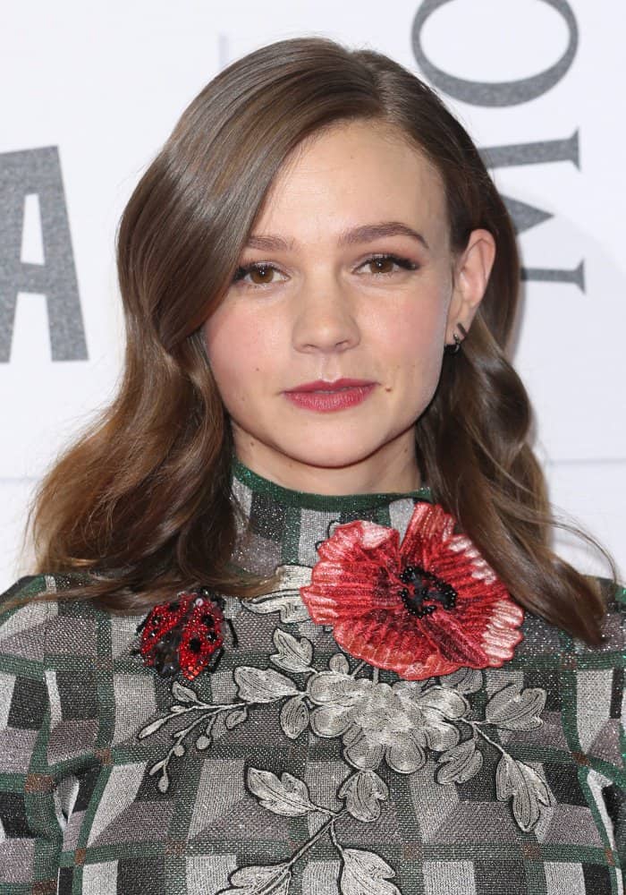 Carey Mulligan's dress features intricate floral embroidery, including a striking red poppy and a ladybug detail, set against a geometric checkered pattern, creating a unique blend of classic and contemporary design elements