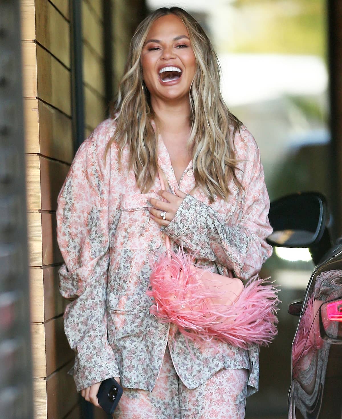 Chrissy Teigen shows everyone how happy she is with Bottega Veneta's pink beak feather-trimmed studded leather clutch