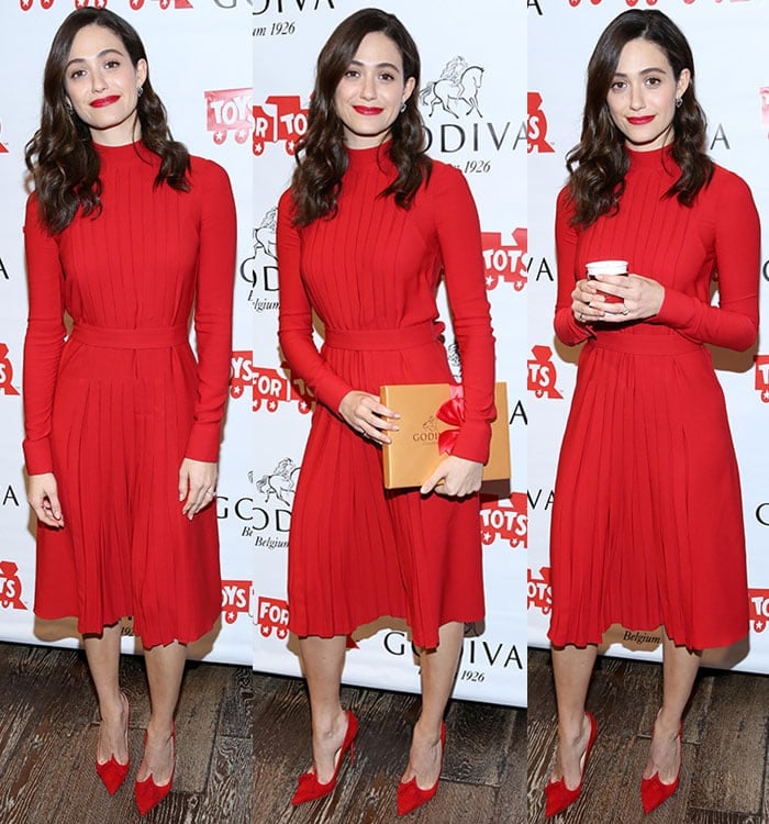 Emmy Rossum holds a box of Godiva chocolates and a cup of Godiva hot chocolate in a red pleated Salvatore Ferragamo dress