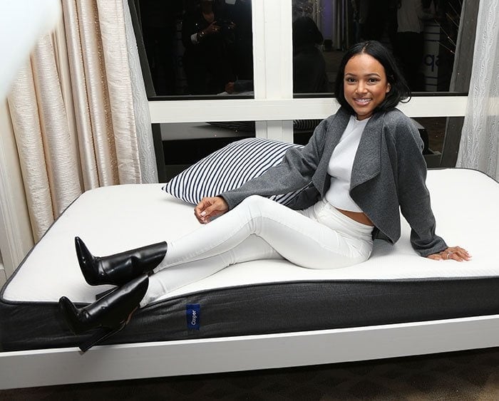 Karrueche Tran posiert auf einer Casper-Matratze und trägt dabei ein Crop-Top und High-Waisted-Jeanstaillierte Jeans