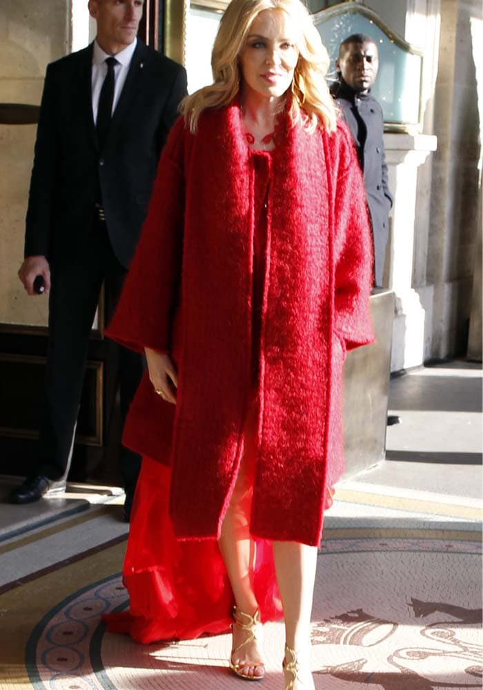 Kylie Minogue wears a red coat and a red dress with a gold pair of "Lang" heels