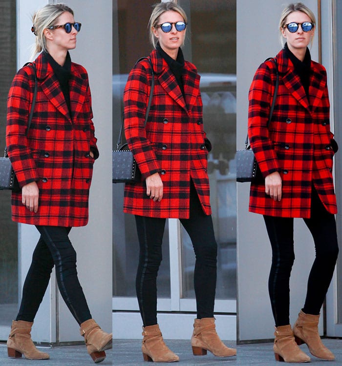 Nicky Hilton wears a red-and-black plaid coat with black leggings and a pair of Saint Laurent booties