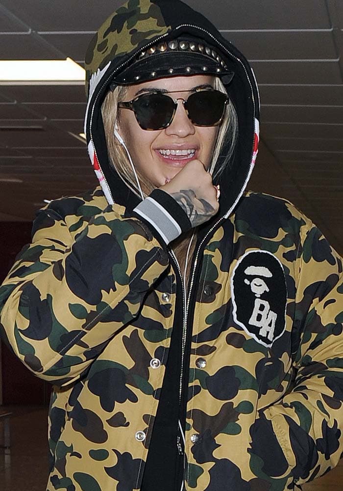 Rita Ora ditches the makeup and hides her hair under a hat as she arrives at London's Heathrow Airport