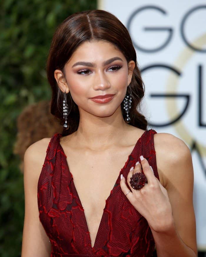 Zendaya radiates sophistication in a close-up of her deep red Marchesa gown, complemented by elegant drop earrings and a bold statement ring, at the 2016 Golden Globe Awards