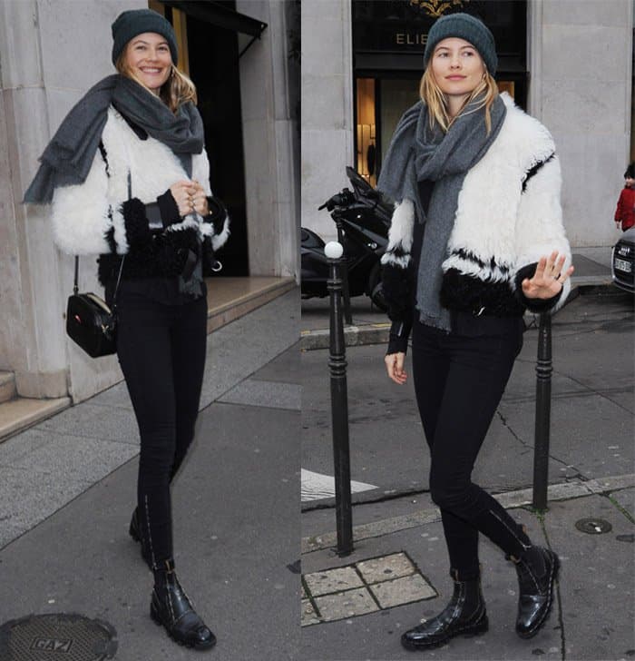 Behati Prinsloo sports a chic winter ensemble featuring a black and white fur jacket, black skinny jeans, ankle boots, a gray beanie, and scarf, completing the look with a small crossbody bag