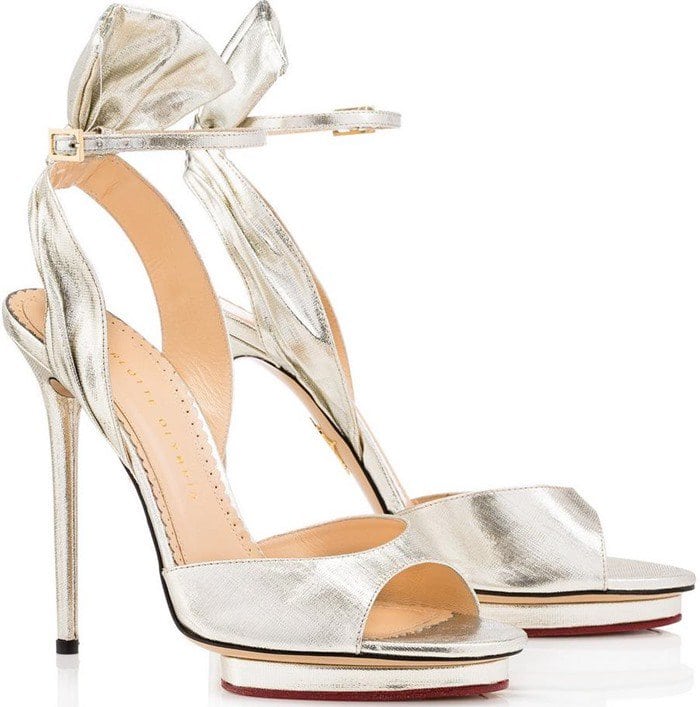 A bow-like accent at the ankle strap balances out the island platform of a fanciful peep-toe sandal fashioned from silvery lamé fabric and finished with a towering stiletto heel