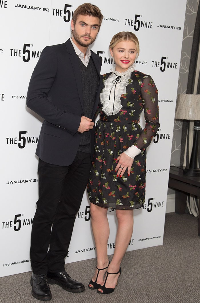 Chloë Grace Moretz and co-star Alex Roe pose together at The 5th Wave photocall in London, with Chloë wearing a floral Erdem dress and Casadei t-strap sandals