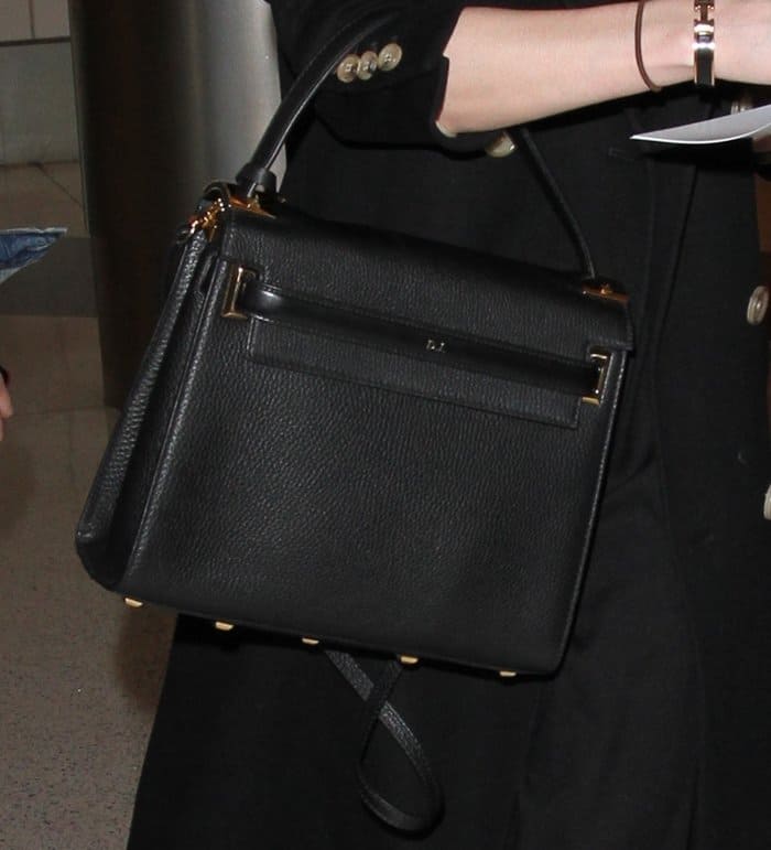 Dakota Johnson carries her personalized black Valentino My Rockstud satchel, subtly embossed with her initials ‘D.J.’—a chic touch to her all-black airport ensemble
