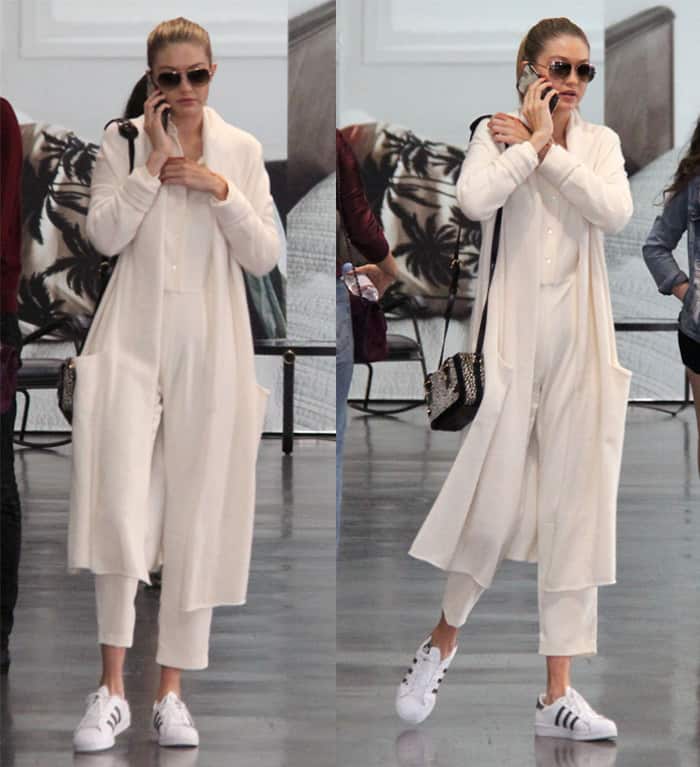 Gigi Hadid in an all-white ensemble featuring a long cardigan, cropped pants, and Adidas sneakers, accessorized with sunglasses and a studded handbag