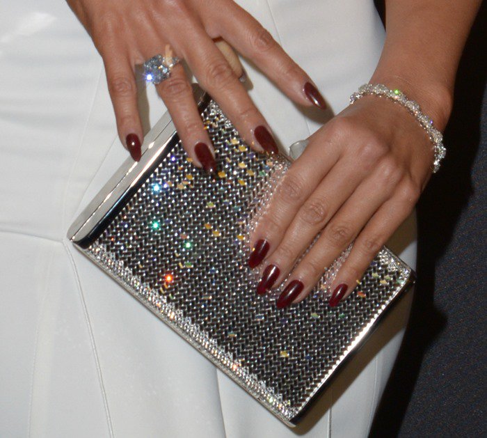 Jennifer Lopez's look is elevated with a dazzling Judith Leiber crystal clutch, a sparkling diamond ring, a delicate bracelet, and her bold dark red manicure that adds a touch of drama