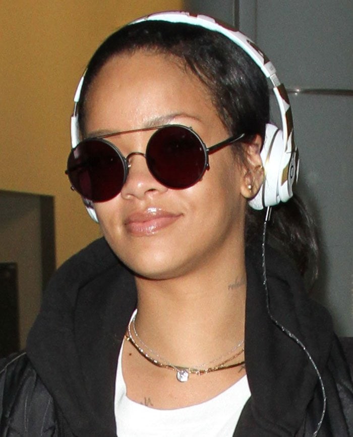 Rihanna uses a pair of headphones to keep her hair back as she arrives at Los Angeles International Airport