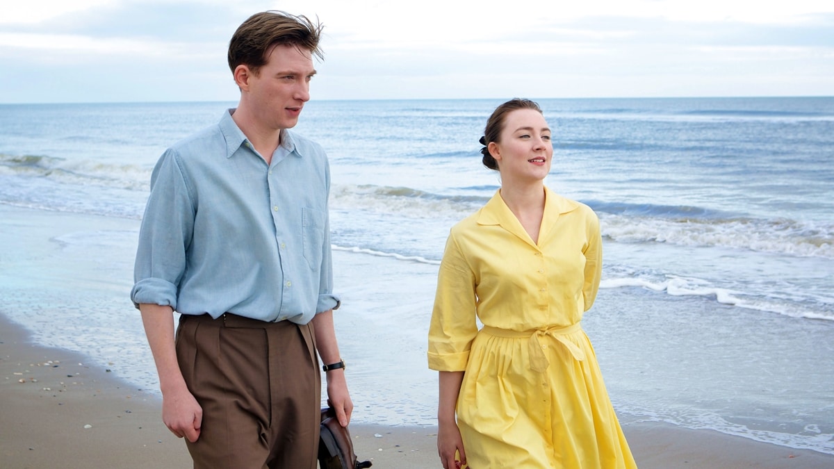 Saoirse Ronan as Eilis Lacey and Domhnall Gleeson as Jim Farrell share a quiet moment by the sea in Brooklyn (2015), adapted from Colm Tóibín’s acclaimed novel
