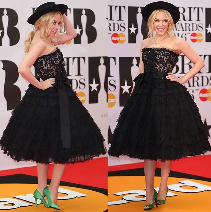 Kylie Minogue stuns in a playful black lace Dolce & Gabbana dress, paired with bold emerald green satin pumps and a wide-brimmed hat at the 2016 BRIT Awards