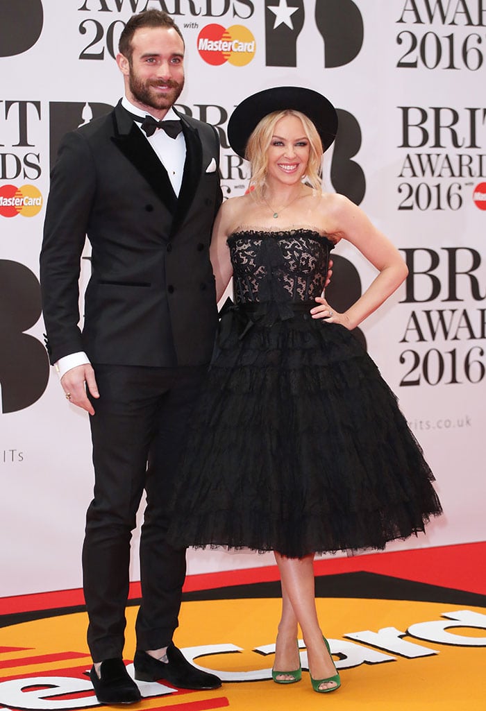 Kylie Minogue and her fiancé Joshua Sasse make a stylish pair on the red carpet at the 2016 BRIT Awards, with Kylie in a dramatic black lace dress by Dolce & Gabbana and Joshua in a classic black tuxedo