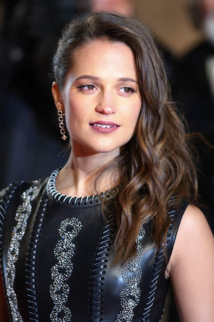 Alicia Vikander stuns in a crystal-embellished leather gown, pairing the bold texture with side-swept waves, radiant makeup, and sparkling drop earrings