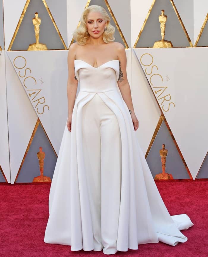 Lady Gaga wears a white pantsuit with an overskirt by Brandon Maxwell at the 88th Annual Academy Awards