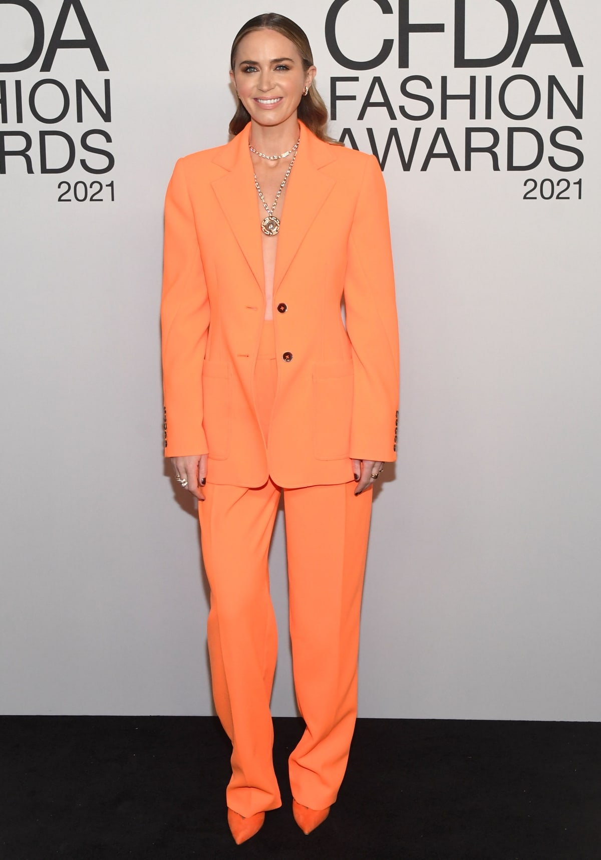 Emily Blunt wears a tangerine Christopher John Rogers Resort 2022 suit and matching Titi Adesa pumps as she hosts the 2021 CFDA Fashion Awards