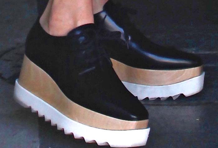 Kendall Jenner is wearing Stella McCartney "Elyse" platform oxfords, a bold and stylish footwear choice featuring black faux leather uppers, thick wooden wedge soles, and serrated white rubber outsoles