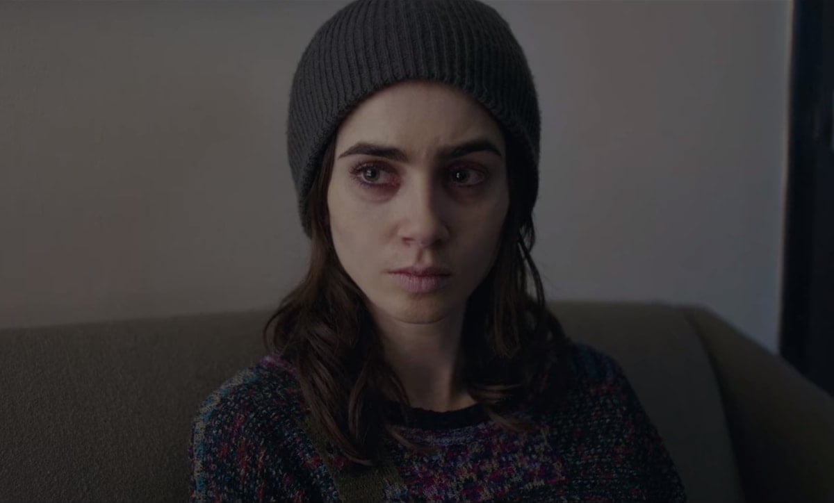 Lily Collins, portraying Ellen in To the Bone, sits solemnly in a multicolored knit sweater and a gray beanie, reflecting the raw emotional depth of her character's struggle with anorexia