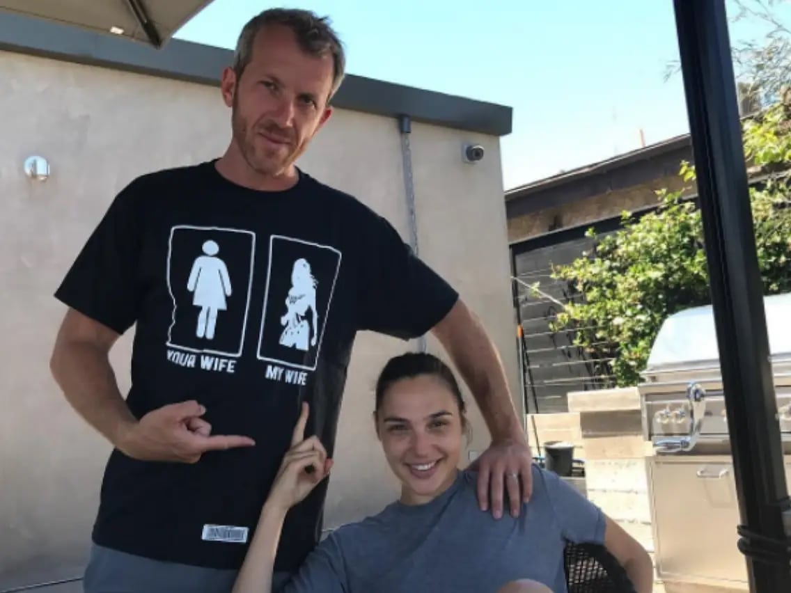 Gal Gadot's husband Yaron Versano wears a t-shirt showing the classic symbol for a women's restroom, captioned "your wife," while the other side has an illustration of Wonder Woman, captioned, "my wife"