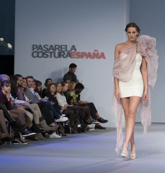 An ethereal asymmetrical mini dress paired with a delicate sheer shawl graces the runway at Pasarela Costura España
