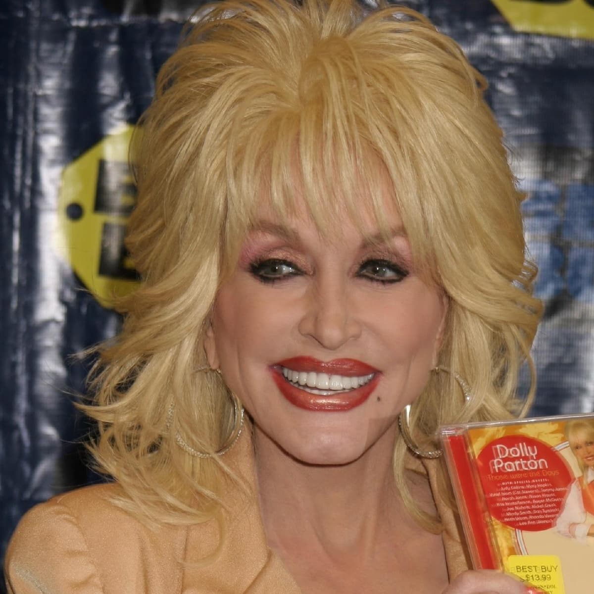 Dolly Parton beams while promoting her album Those Were the Days at a Best Buy event, showcasing her signature blonde hair, bold makeup, and radiant smile
