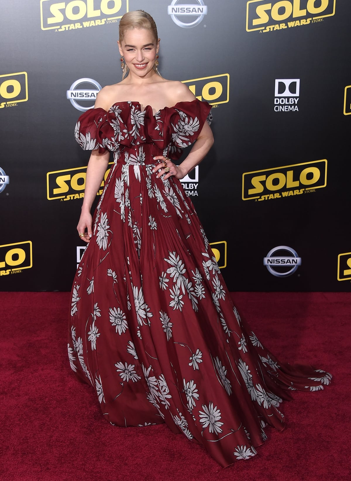 Emilia Clarke in a Valentino Spring 2018 Couture off-the-shoulder red gown with white flowers at the premiere of Disney Pictures and Lucasfilm’s Solo: A Star Wars Story