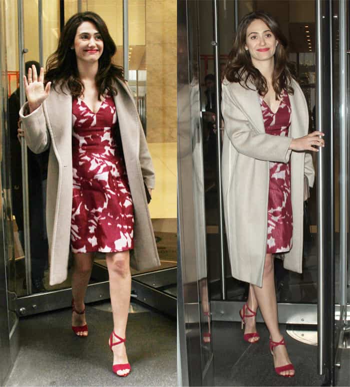 Emmy Rossum radiates effortless femininity in a floral red dress paired with a soft beige coat and matching red heels, creating a perfectly balanced and chic ensemble