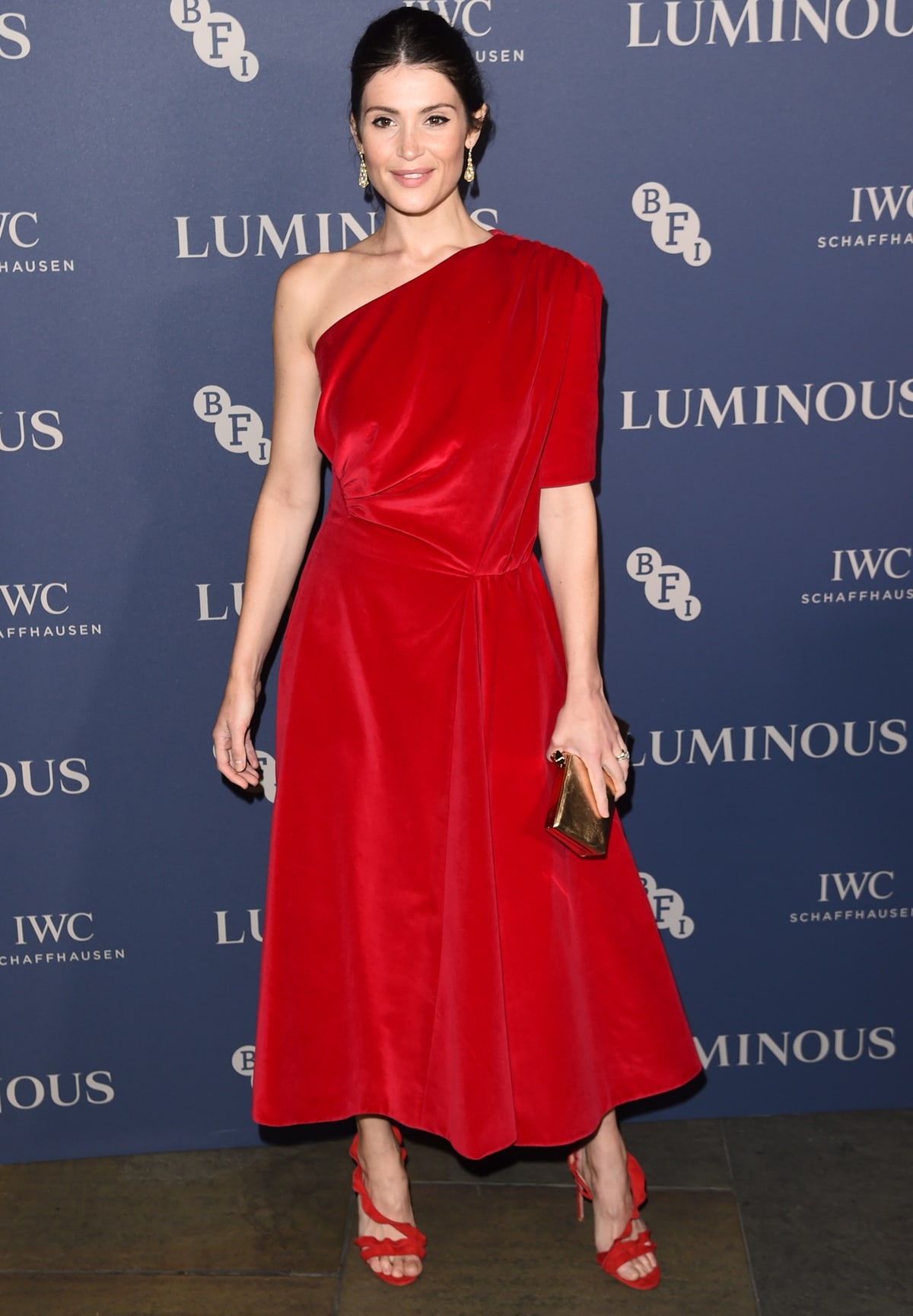 Gemma Arterton wears a red one-shouldered Emilia Wickstead velvet dress paired with Aquazzura ruffled suede sandals at the BFI Luminous Fundraising Gala