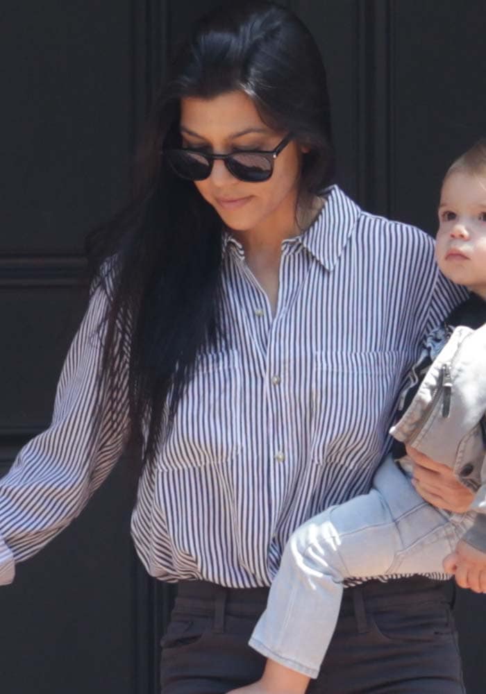 Kourtney Kardashian stylishly pairing a striped button-down with Saint Laurent SL 93 sunglasses while carrying her son, Reign