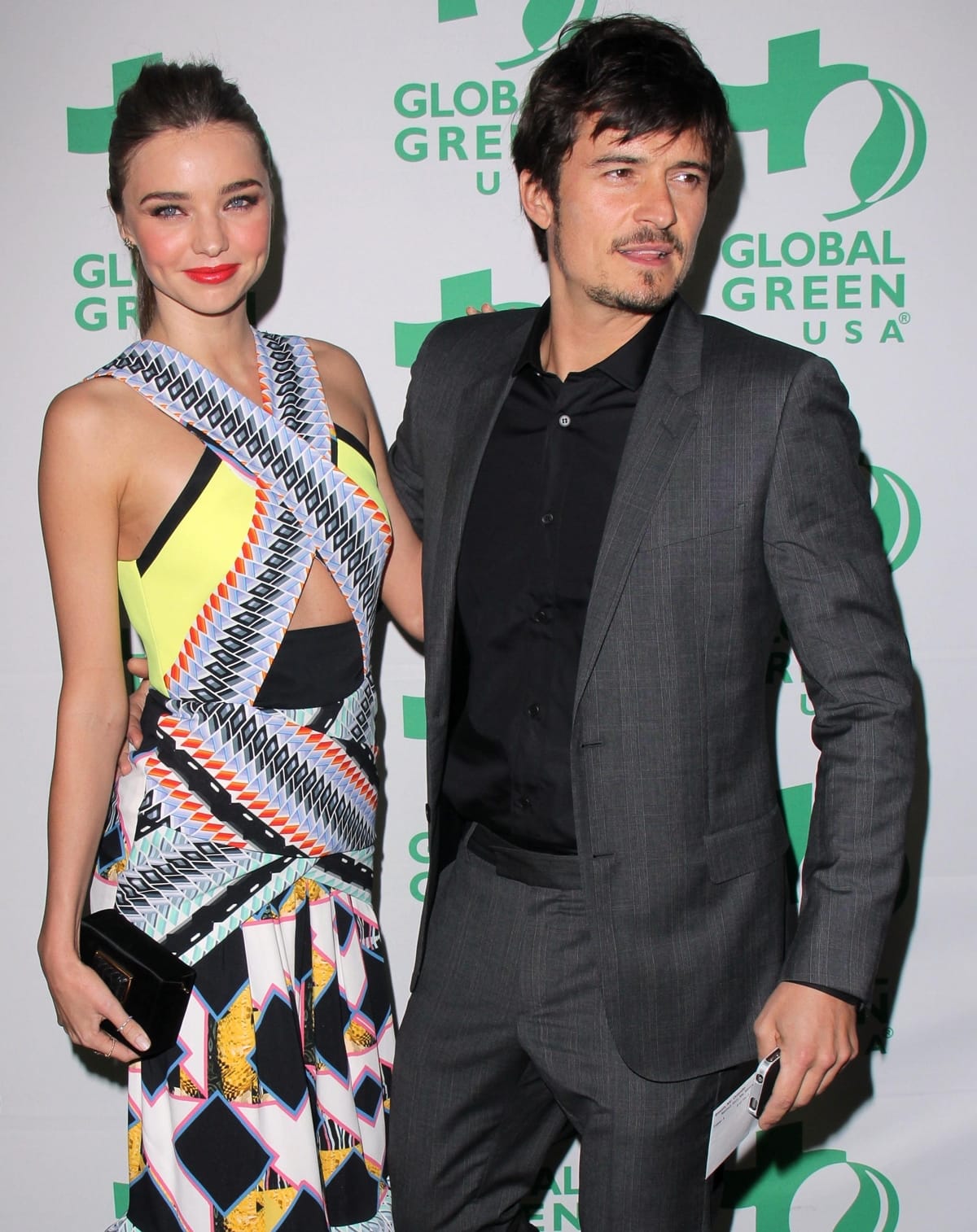 Miranda Kerr stuns in a vibrant geometric-print cutout dress, while Orlando Bloom keeps it classic in a charcoal suit with a black button-up