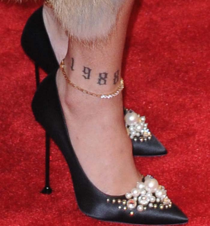 Rihanna completes her look with elegant black satin pumps embellished with pearls and gold studs, perfectly paired with a delicate anklet, showcasing her edgy '1988' tattoo