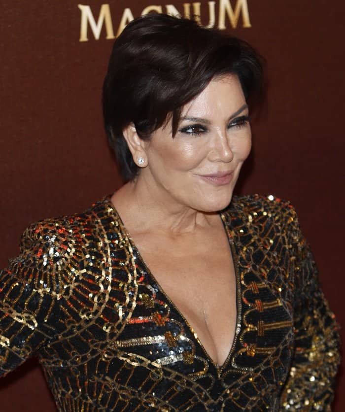 Kris Jenner complements her black and gold Balmain sequin dress with elegant earrings, a chic short hairstyle, and her signature smoky eye makeup