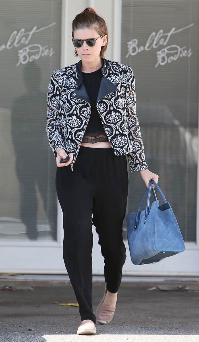 Kate Mara rocks a chic ensemble of black sweatpants, a cropped top, a statement printed jacket, and stylish loafers, making post-ballet look effortlessly stylish