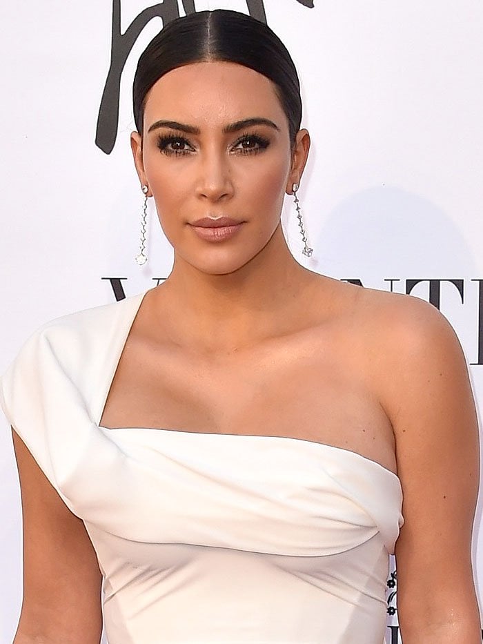 Kim Kardashian sporting a slicked-down center-parted hairdo, heavy lashes, and dangling diamond earrings