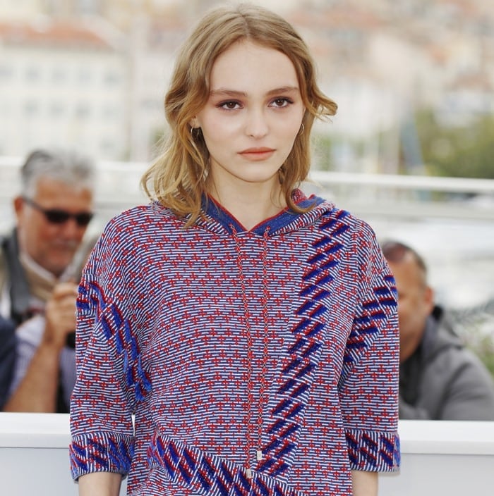 Lily-Rose Depp wears a blue, red, and white hooded top with denim panels
