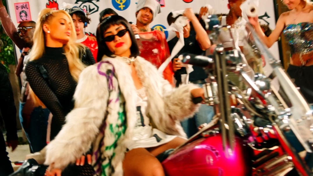 Demi Lovato and Paris Hilton are sitting together on the back of a motorcycle in the music video for “Substance,” a single from her album Holy Fvck