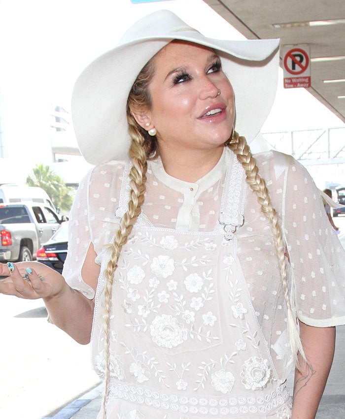 Kesha channels boho-chic vibes in a sheer embroidered white outfit, complete with a floppy hat and braided pigtails, while spotted at Los Angeles International Airport