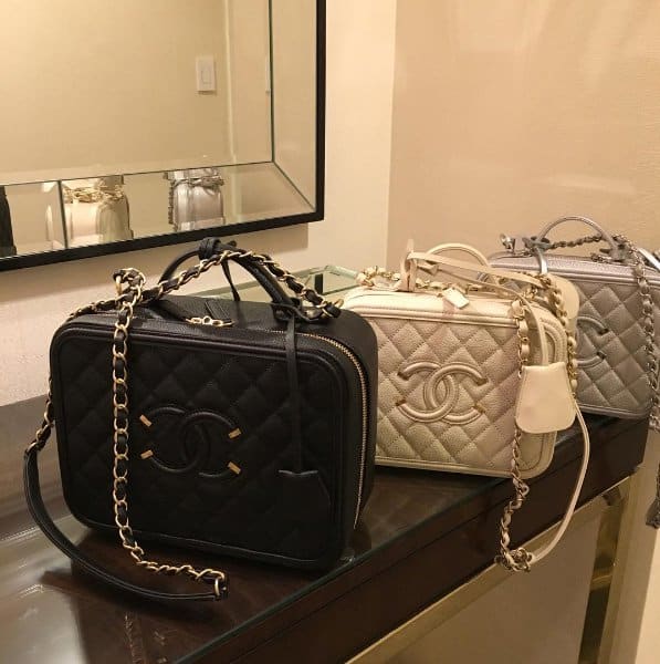 A row of quilted Chanel Vanity Cases in black, ivory, and metallic silver—each featuring the signature CC logo, chain strap, and structured box silhouette—exudes timeless elegance