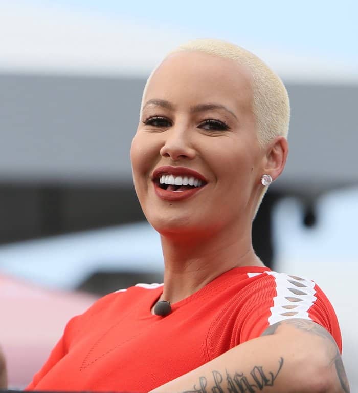 Amber Rose's radiant smile is perfectly complemented by her sparkling diamond stud earrings and bold red lips, highlighting her flawless teeth and confident style
