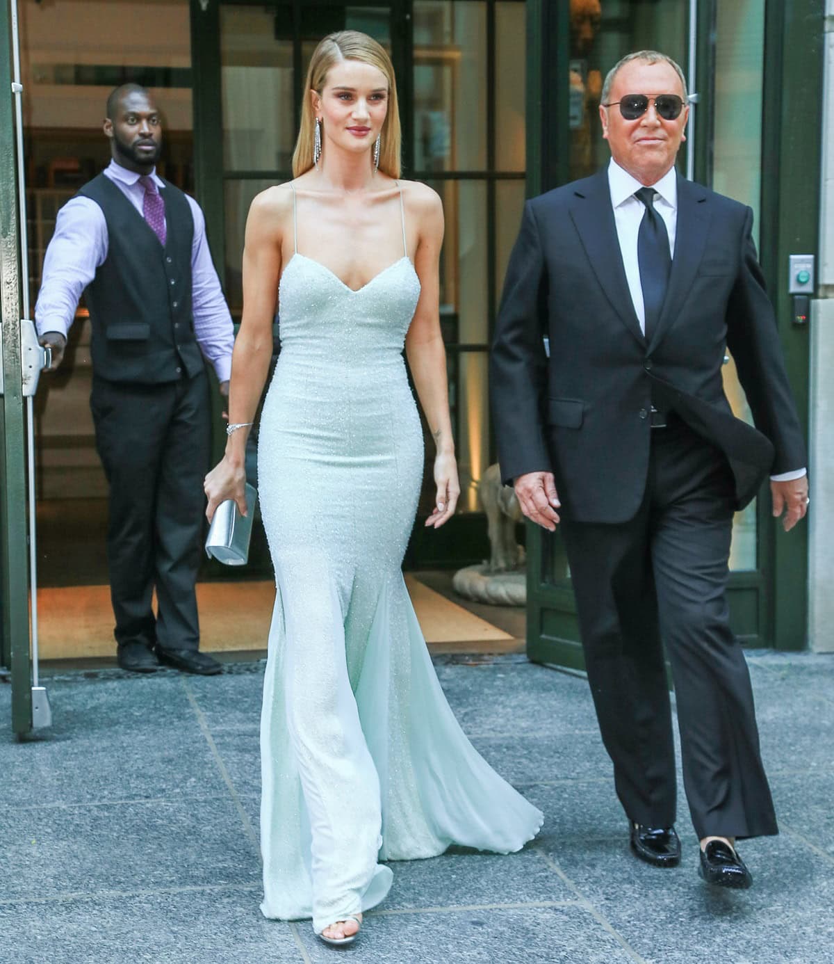 When Rosie Huntington-Whiteley stopped outside, the front slit exposed pale, open-toe platform heels that blended seamlessly with the gown’s icy tone, adding height while keeping the silhouette fluid and uninterrupted