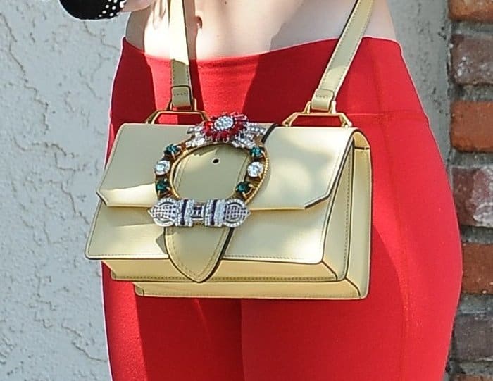 Close-up of Elle Fanning’s pale yellow crossbody bag, featuring a jeweled horseshoe buckle and structured silhouette—resembling the embellished Gucci Dionysus min