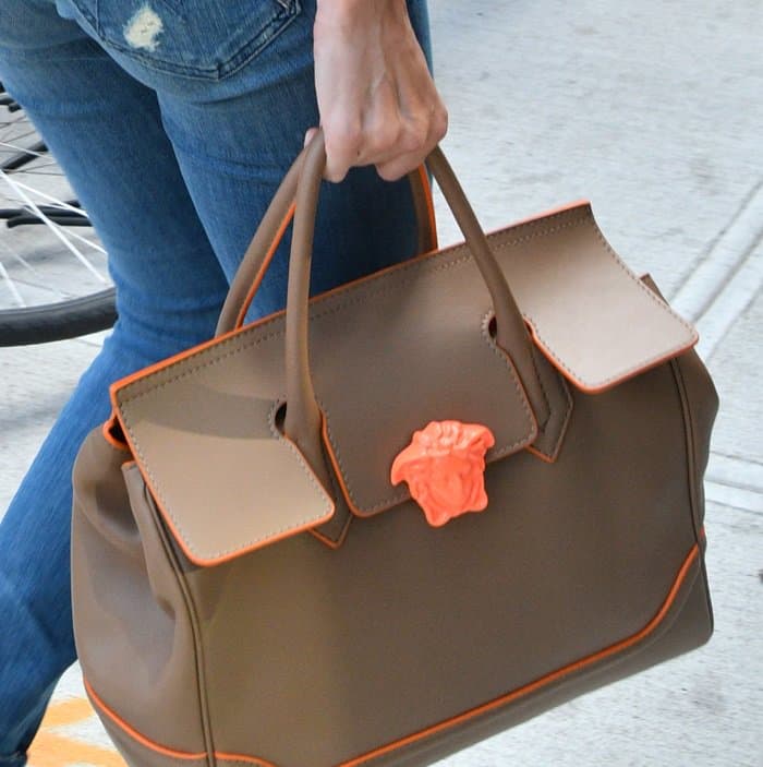 Gigi Hadid adds a pop of contrast to her neutral-toned outfit with the Versace Palazzo Empire tote, featuring a bold orange Medusa emblem and trim that elevate its structured silhouette