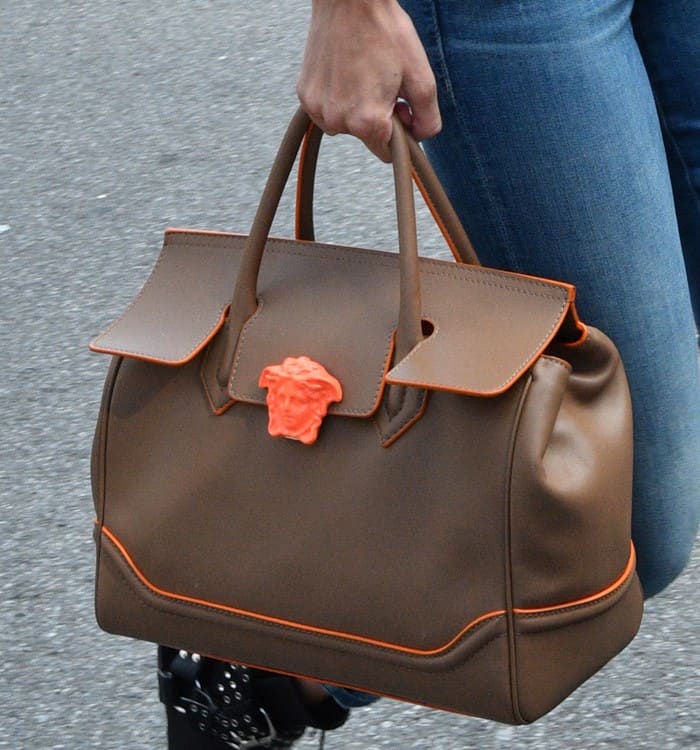 Gigi Hadid adds a pop of contrast to her neutral-toned outfit with the Versace Palazzo Empire tote, featuring a bold orange Medusa emblem and trim that elevate its structured silhouette