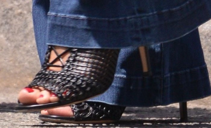 Heidi Klum flaunts a bold red pedicure in intricate woven Gianvito Rossi "Marnie" lace-up mules, peeking out perfectly from beneath her flared jeans