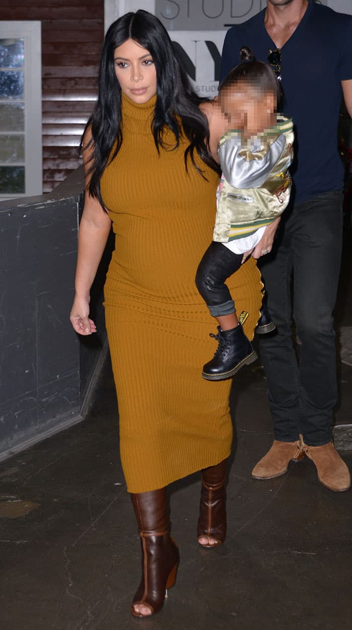 Kim Kardashian exudes confidence in a mustard ribbed dress that hugs her pregnancy curves, paired with sleek brown open-toe boots, while effortlessly carrying North West by her side