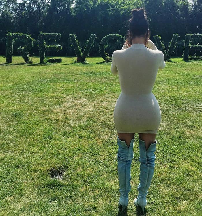 The back of Kim Kardashian's curvy form in a Trois x Revolve 'Campbell' beige knit dress and Yeezy ripped denim thigh-high boots