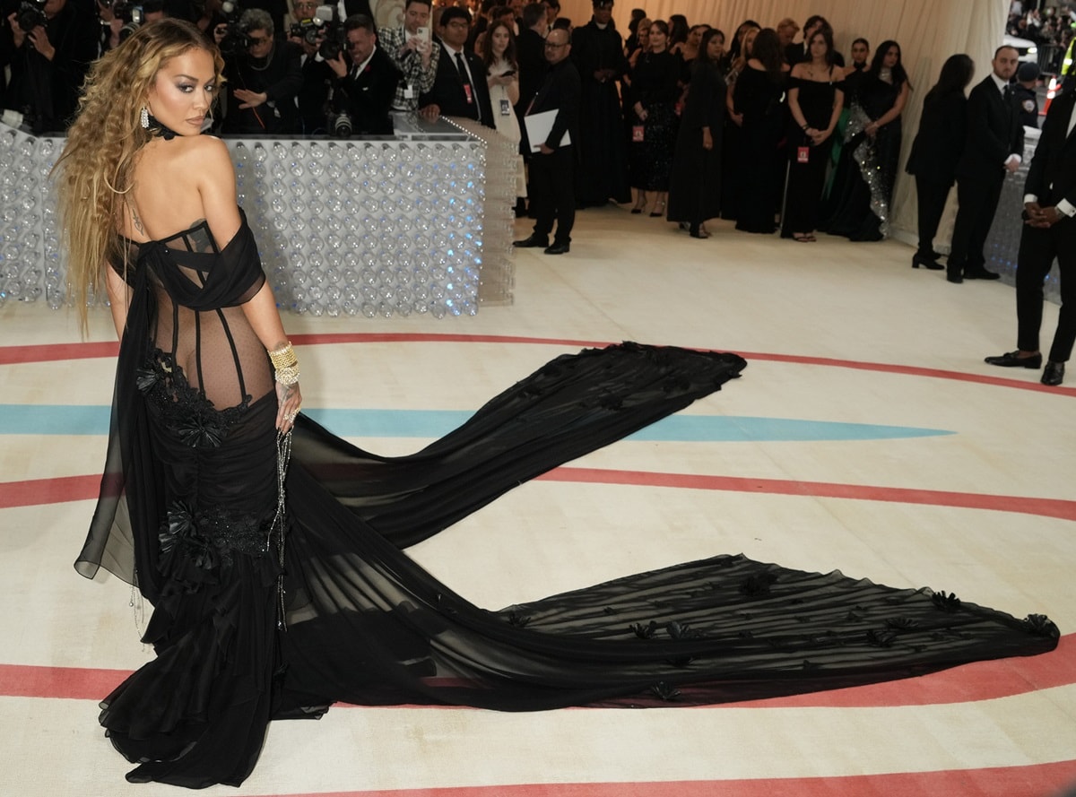 Rita Ora turned heads in a stunning black Prabal Gurung gown that showcased sheer paneling on her torso, tulle-like 3D floral details, and a long side train, all accentuating her edgy style at the 2023 Costume Institute Benefit celebrating “Karl Lagerfeld: A Line of Beauty” at the Metropolitan Museum of Art